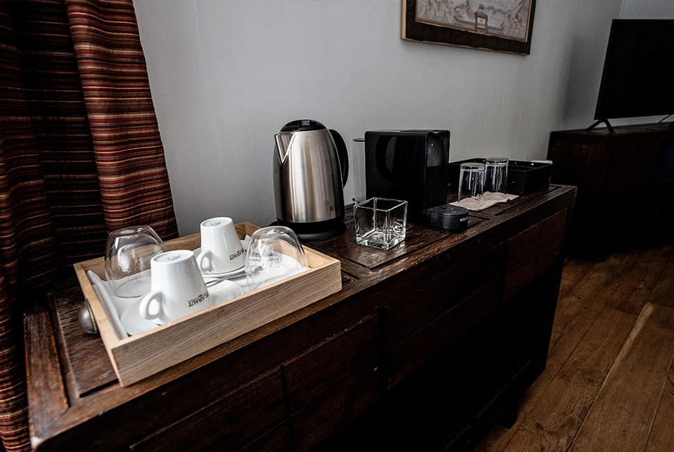 Un buffet présentoir avec un plateau en bois sur lequel il y a des verres et des tasses dans une chambre du Domaine de Béronsart