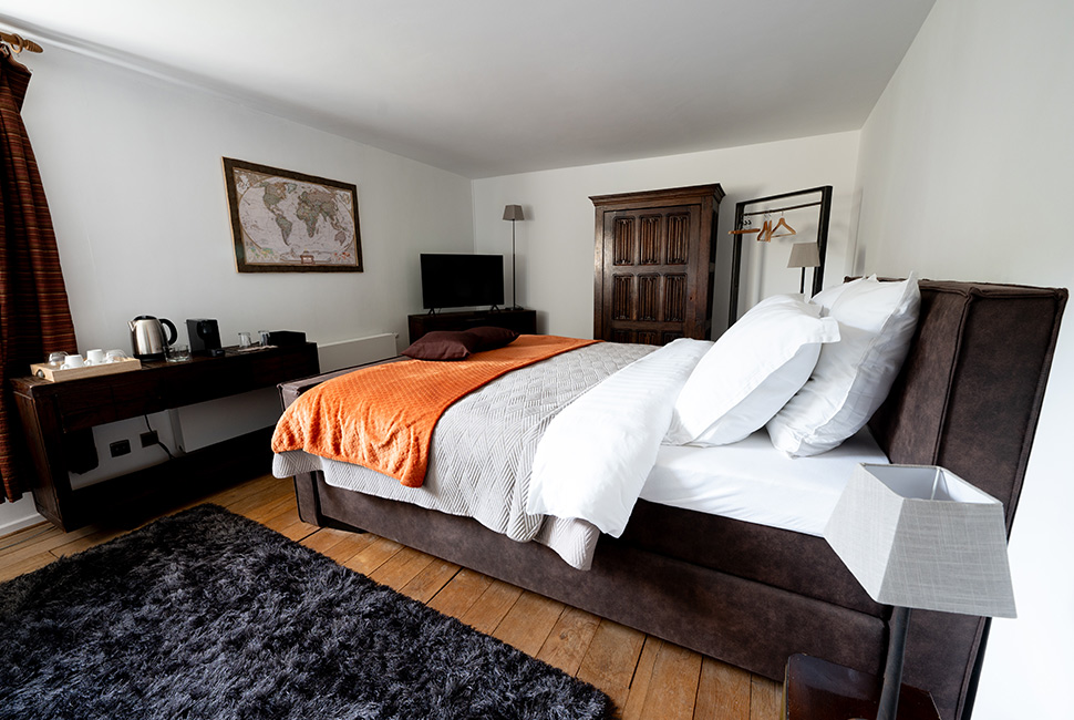 Une chambre du Domaine de Béronsart avec un grand lit, un grand tapis, une armoire brune, un cadre et le parquet en bois