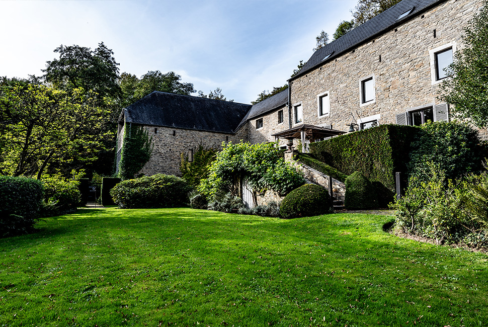 Le Moulin en pierre du Domaine de Béronsart avec un beau gazon à l'avant de la bâtisse et des plantes vertes