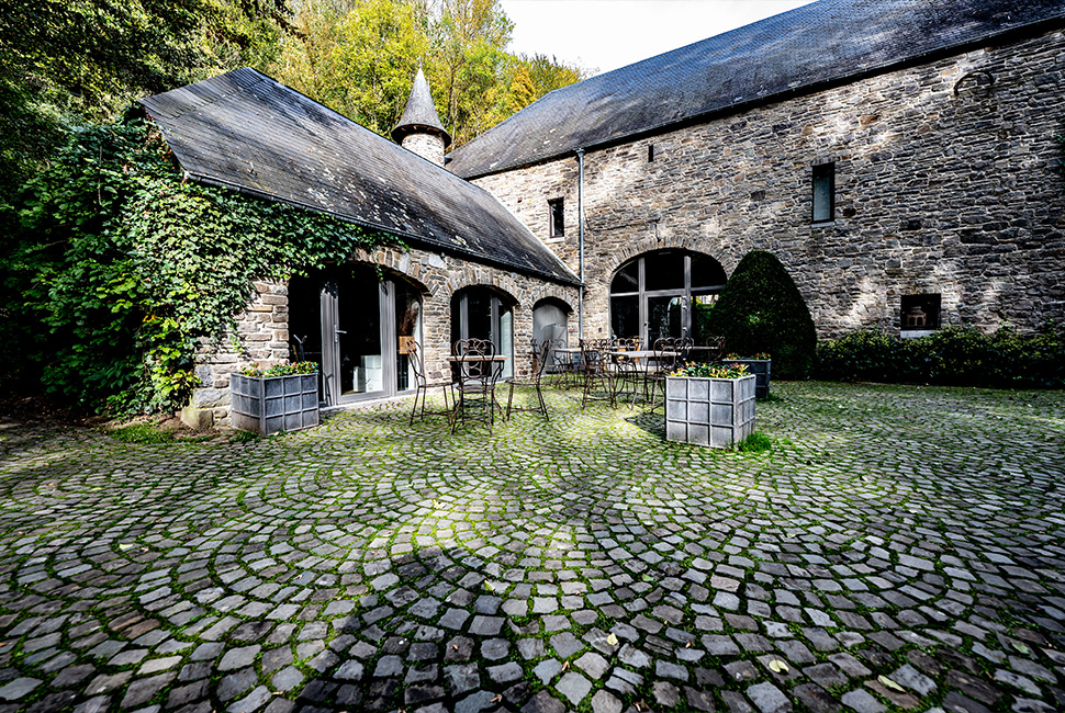 La cour extérieur en pavé du Moulin du Domaine de Béronsart avec de jolies tables en fer forgé et des bacs à plantes