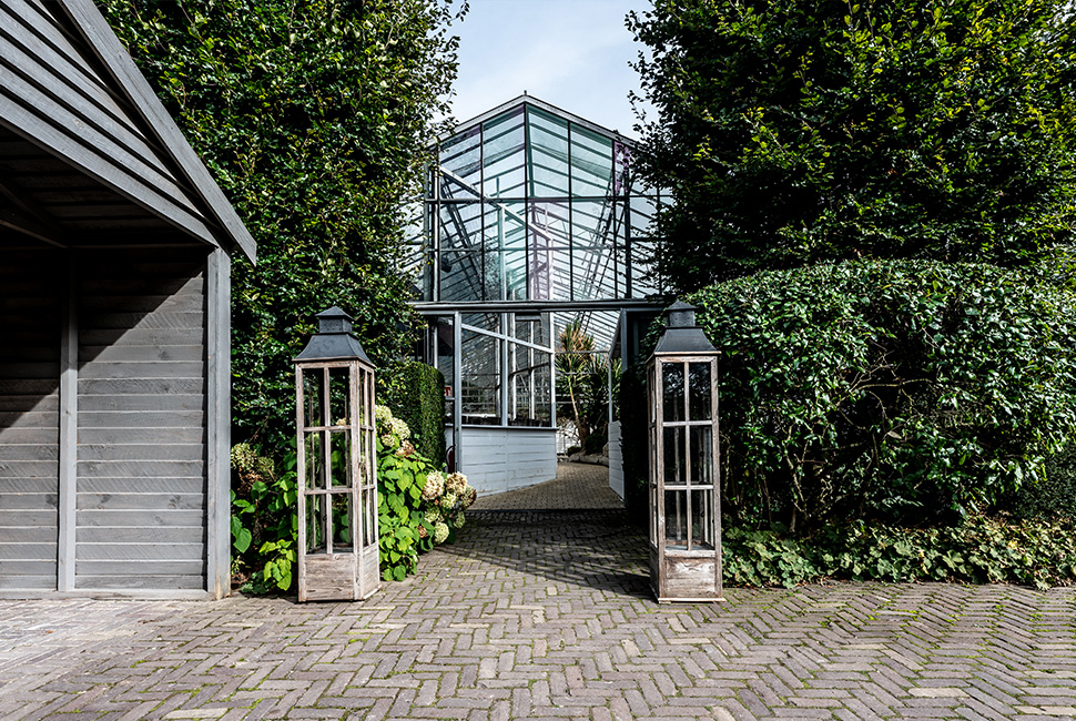 L'entrée de la Serre du Domaine de Béronsart avec des grandes haies, des lampes, des fleurs et des pavés en briques