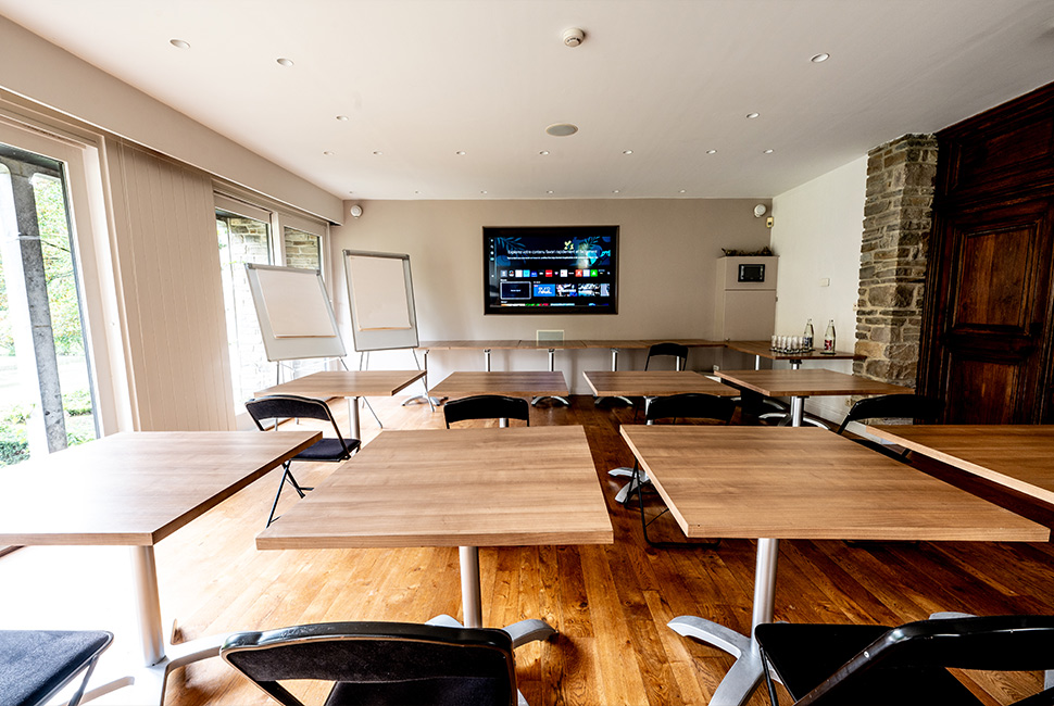 Salle de séminaire du Domaine de Béronsart avec des tables individuelles, des tableaux blancs et une grande télévision