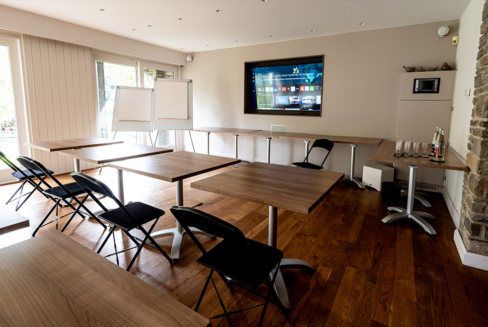 Salle de séminaire du Domaine de Béronsart qui comporte des tables individuelles, des tableaux blancs et une grande télévision