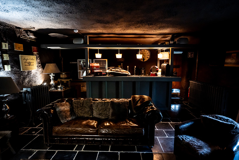Salle de réception du Domaine de Béronsart avec un bar, des fauteuils en cuir foncé et des luminaires